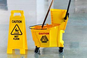 Yellow wet floor sign and matching yellow mop bucket with a mop handle, photographed on a glossy floor.